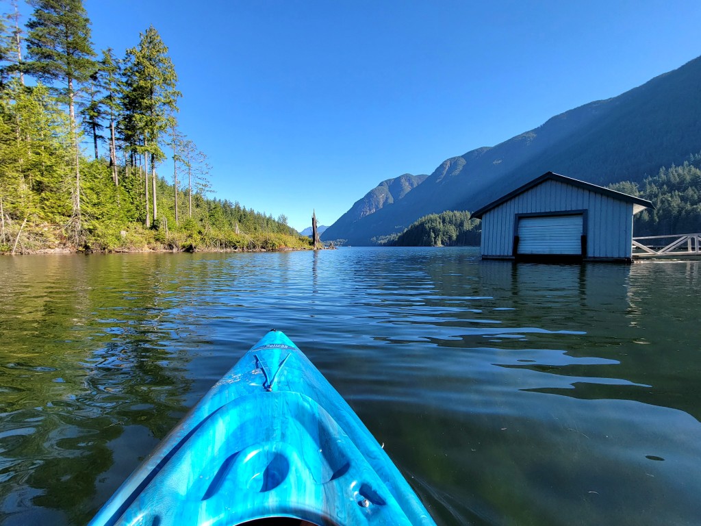 View from a blue kayak on Buntzen Lake with mountains and a lakeside structure